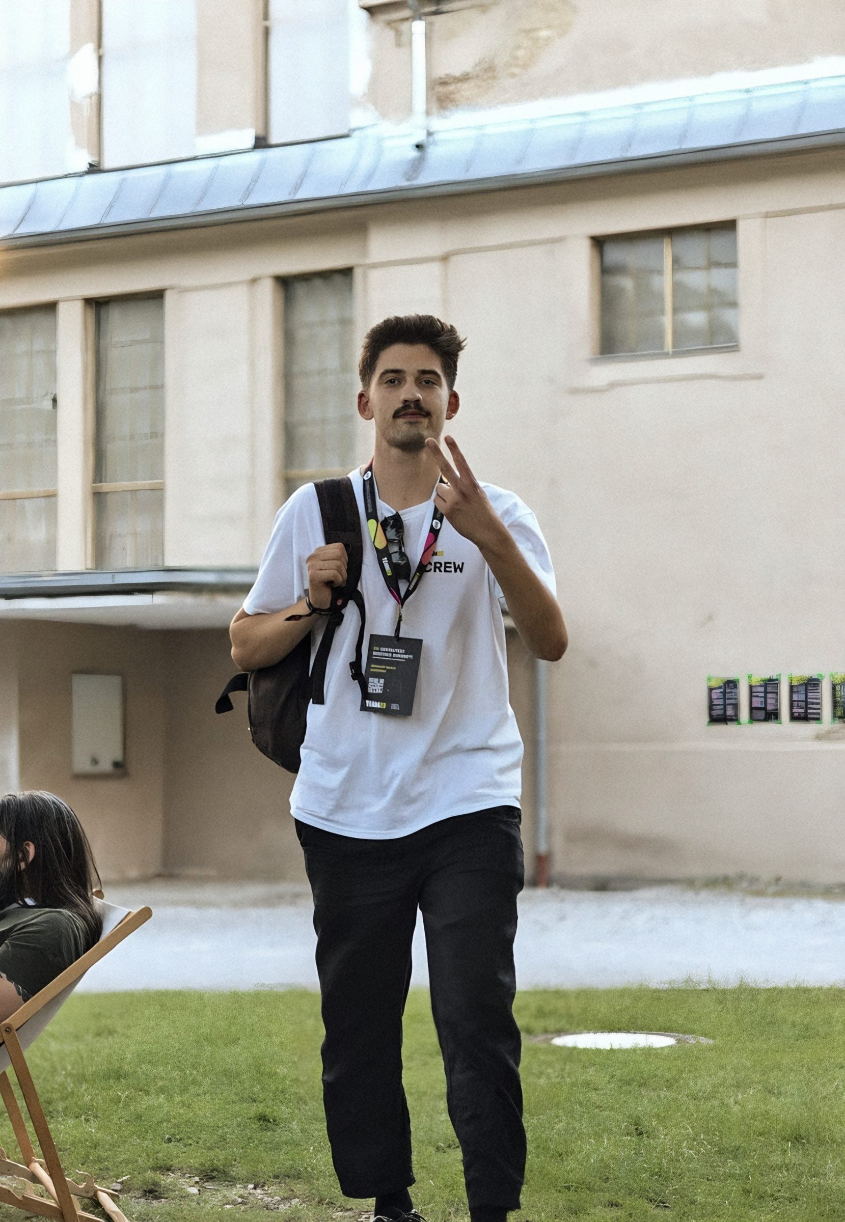 Erik in a white TEAM23 crew shirt with a backpack and badge, smiling and making a peace sign